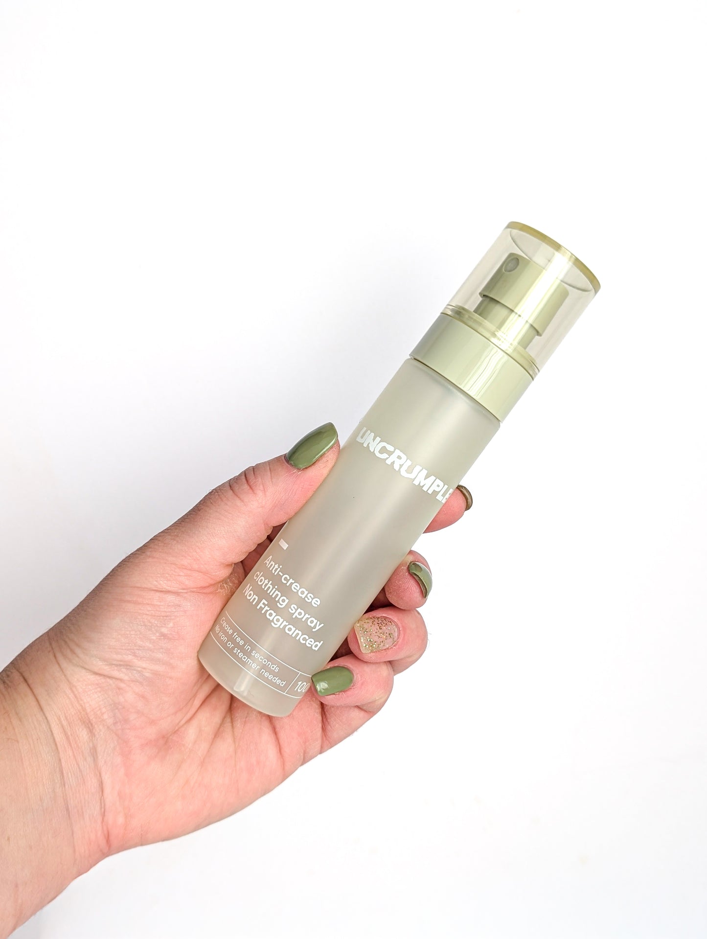 Hand holding a travel-sized bottle of Uncrumpled anti-crease spray against a white background