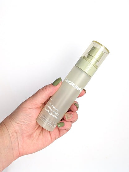 Hand holding a travel-sized bottle of Uncrumpled anti-crease spray against a white background