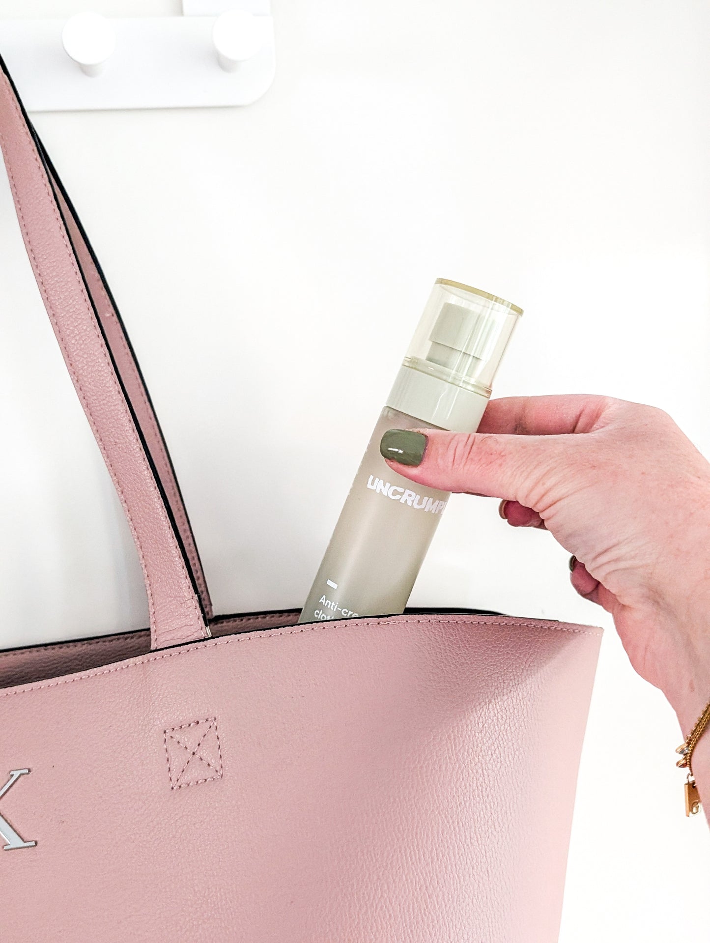 Hand holding a a travel-sized Uncrumpled anti-crease spray bottle, slipping it into a pink handbag on a white background